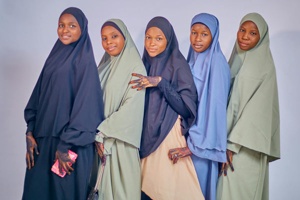 Five women wearing traditional hijabs in different colors posing together in a studio