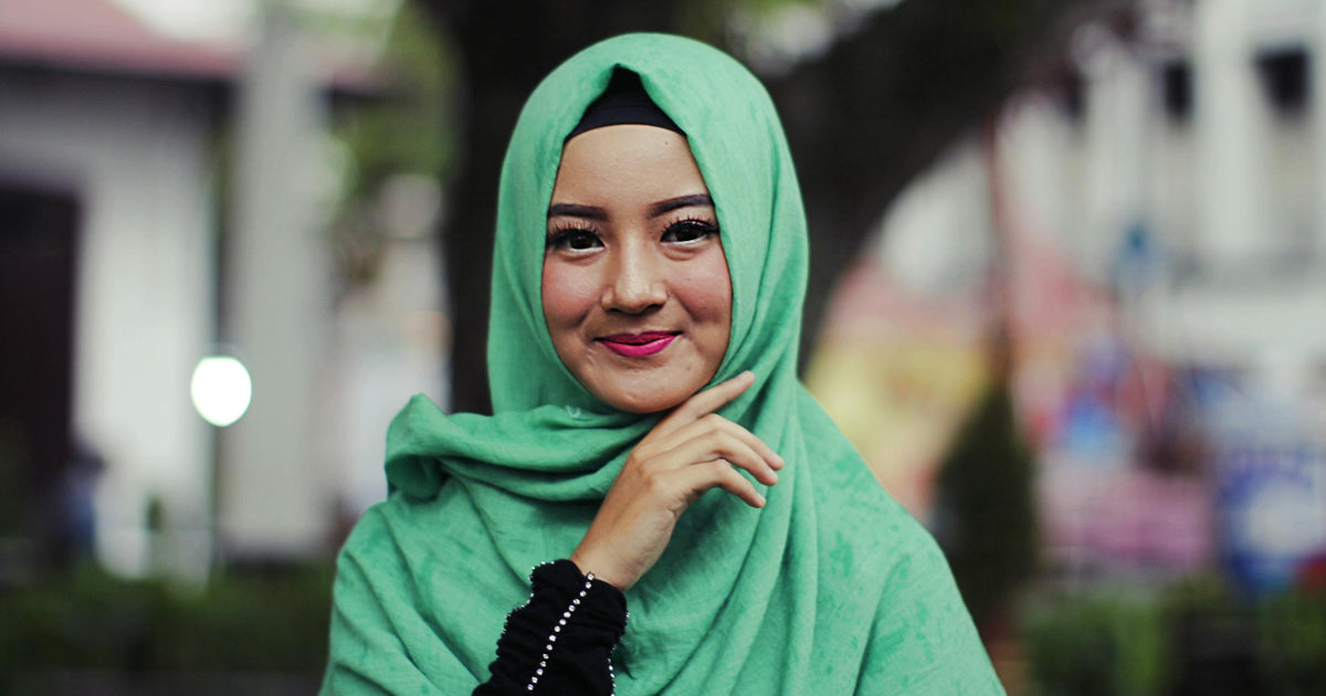 A joyful woman in a green hijab smiling confidently outdoors