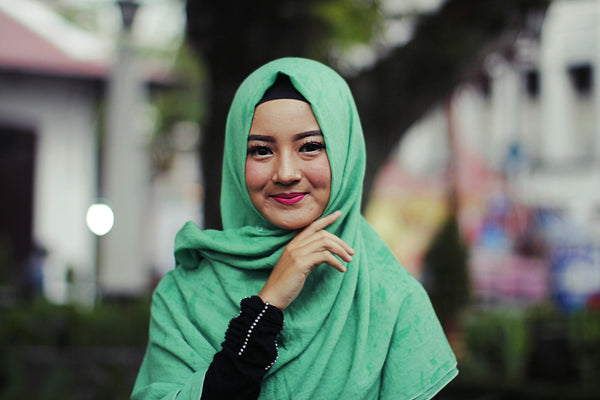 A joyful woman in a green hijab smiling confidently outdoors