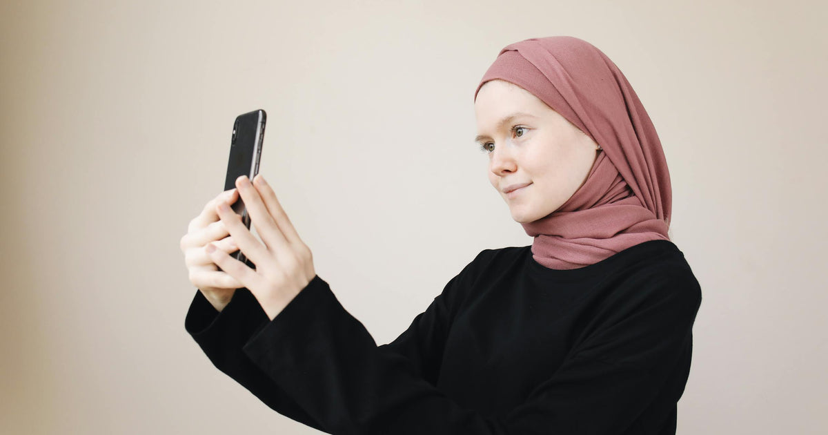 A young Muslim woman in a hijab takes a selfie with her smartphone