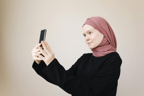A young Muslim woman in a hijab takes a selfie with her smartphone