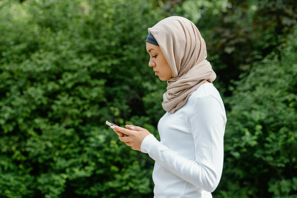 Muslim woman in hijab using a smartphone in a natural outdoor setting