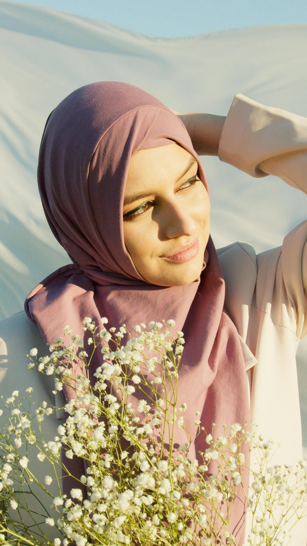 Woman wearing soft mauve hijab in natural golden light with flowers